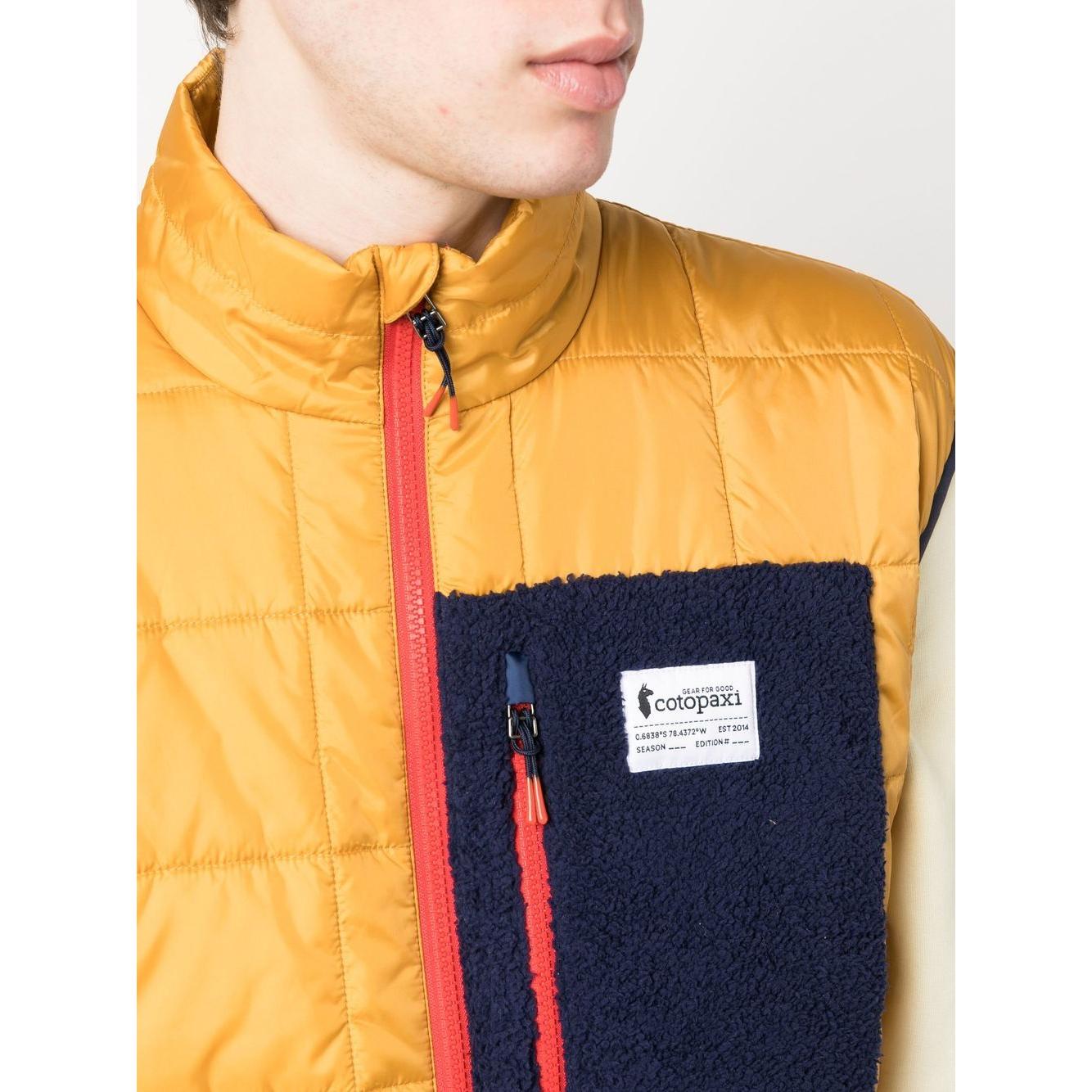 Close-up of a mustard yellow COTOPAXI padded gilet with chest logo patch and front zip fastening, perfect for stylish outdoor wear.