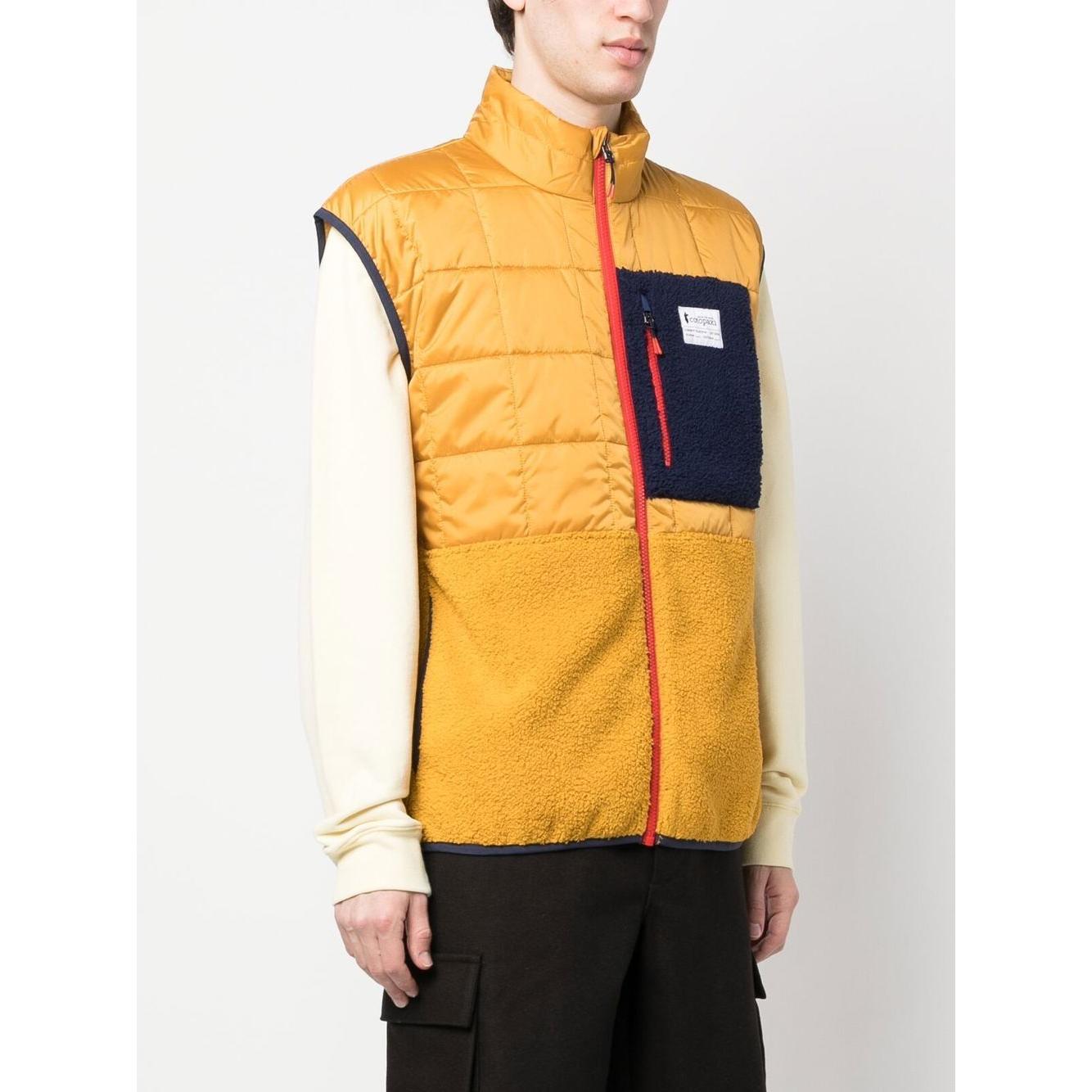 COTOPAXI mustard yellow padded gilet with chest logo patch, front zip, and pockets, worn by a model, showcasing sleeveless design.