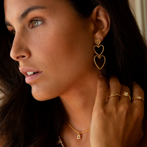 Woman wearing 24KAE JEWELS JEWELRY Mod. 12472Y/52 heart earrings, gold necklace, and rings.
