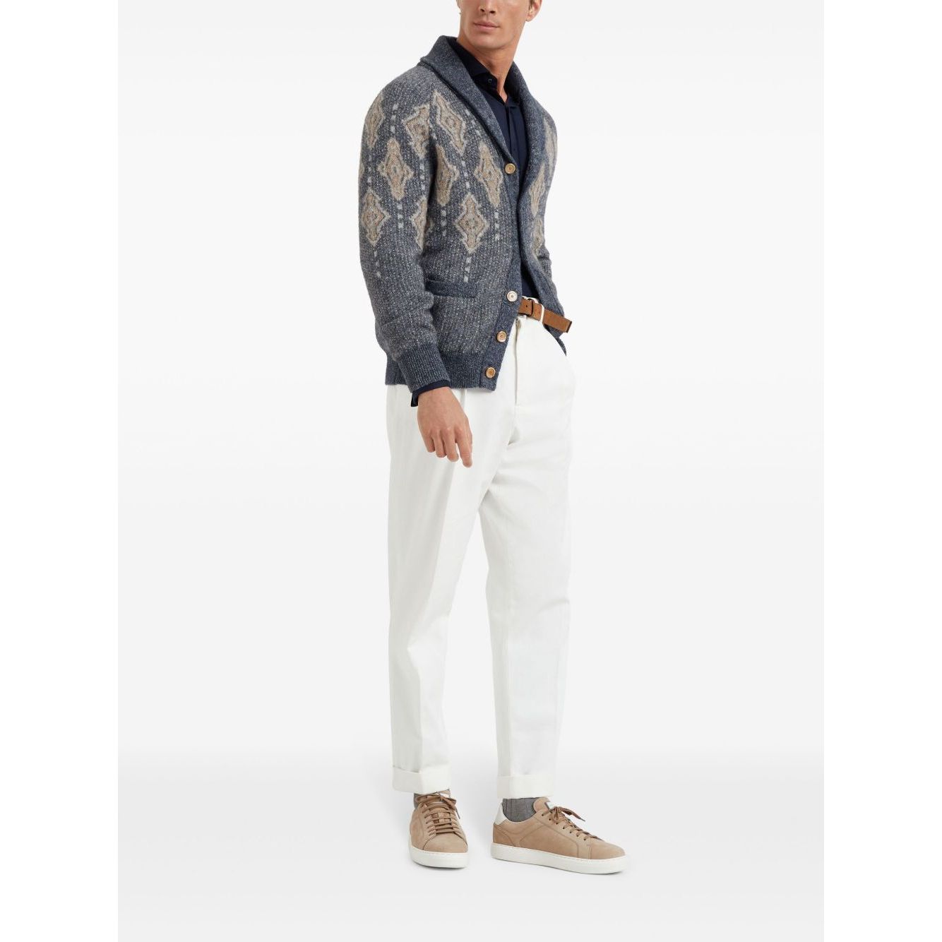 Man wearing patterned blue cardigan with white pants and beige sneakers.