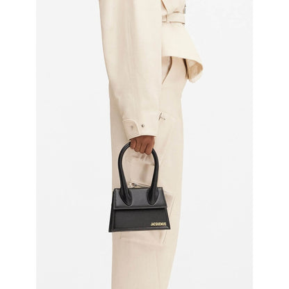 Jacquemus Le Chiquito Moyen Black Bag with gold hardware, shown on model, featuring reinforced handle and magnetic flap closure.