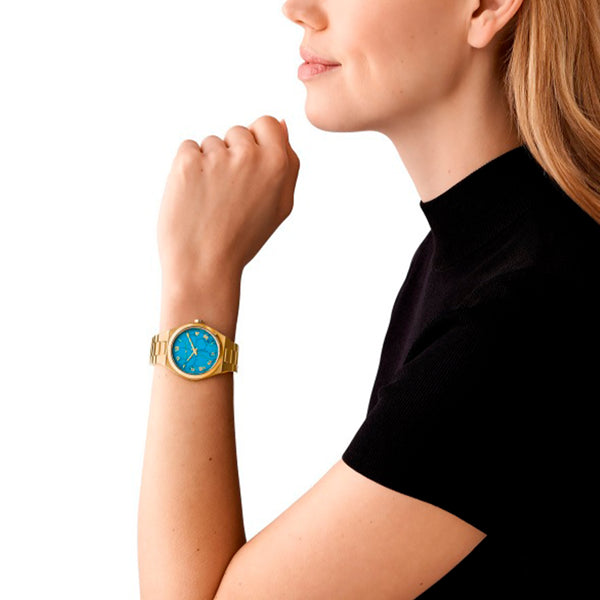 Woman wearing MICHAEL KORS Mod. LENNOX gold wristwatch with blue dial, 39mm case, wrist view, elegant design for ladies.