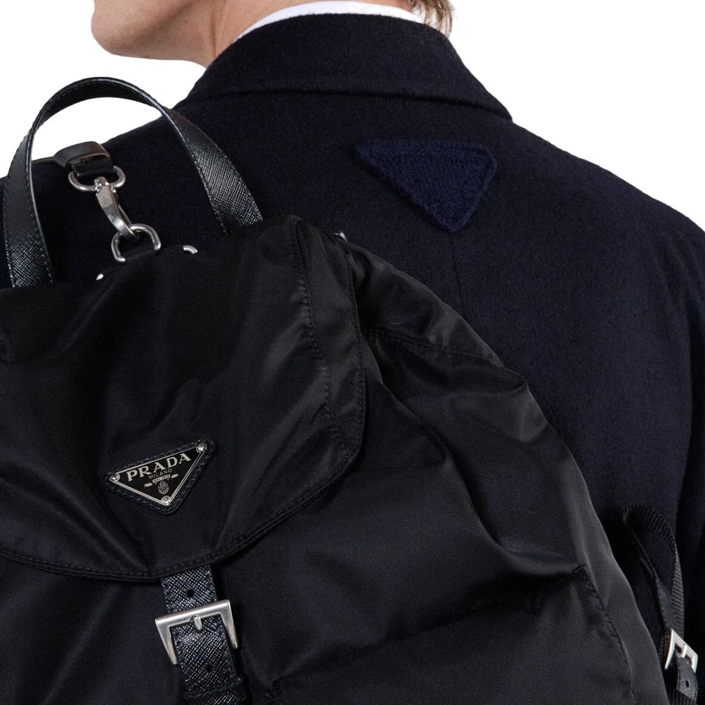 Back view of Prada Blue Wool Coat with triangle logo detail, worn with a black Prada backpack, showcasing high-end fashion design.