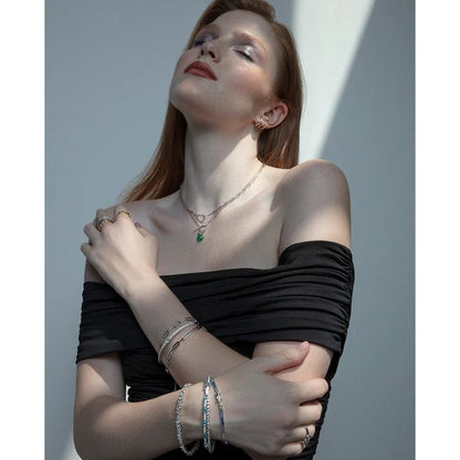 Stylish woman wearing elegant silver jewelry, including bracelets and necklaces, showcasing fashion accessories against a light backdrop.